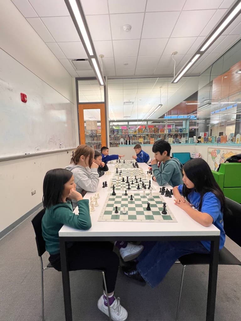 Children practicing chess at ChessTime Academy in a bright, modern library setting.